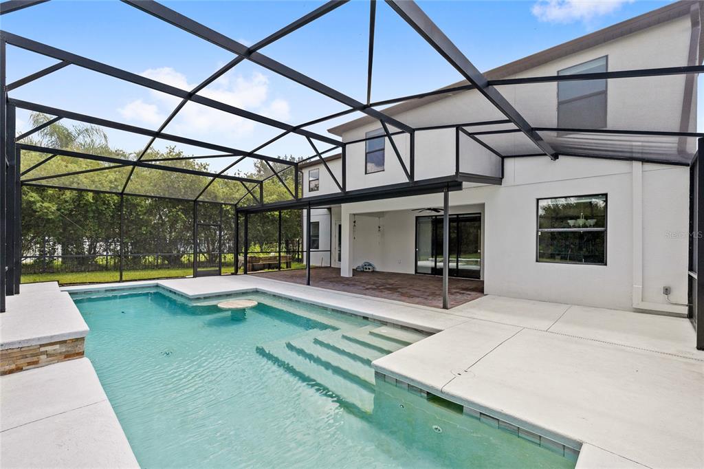 A swimming pool with steps and a table sits inside a screened-in patio area — 2892 SPRING BREEZE WAY, KISSIMMEE, FL