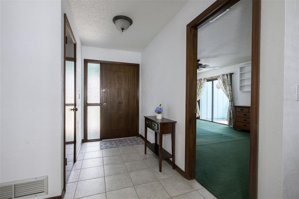 An entryway with tile flooring, a wooden front door, and a doorway leading to carpeted room — 1123 SHERBOURNE WAY, ORMOND BEACH, FL