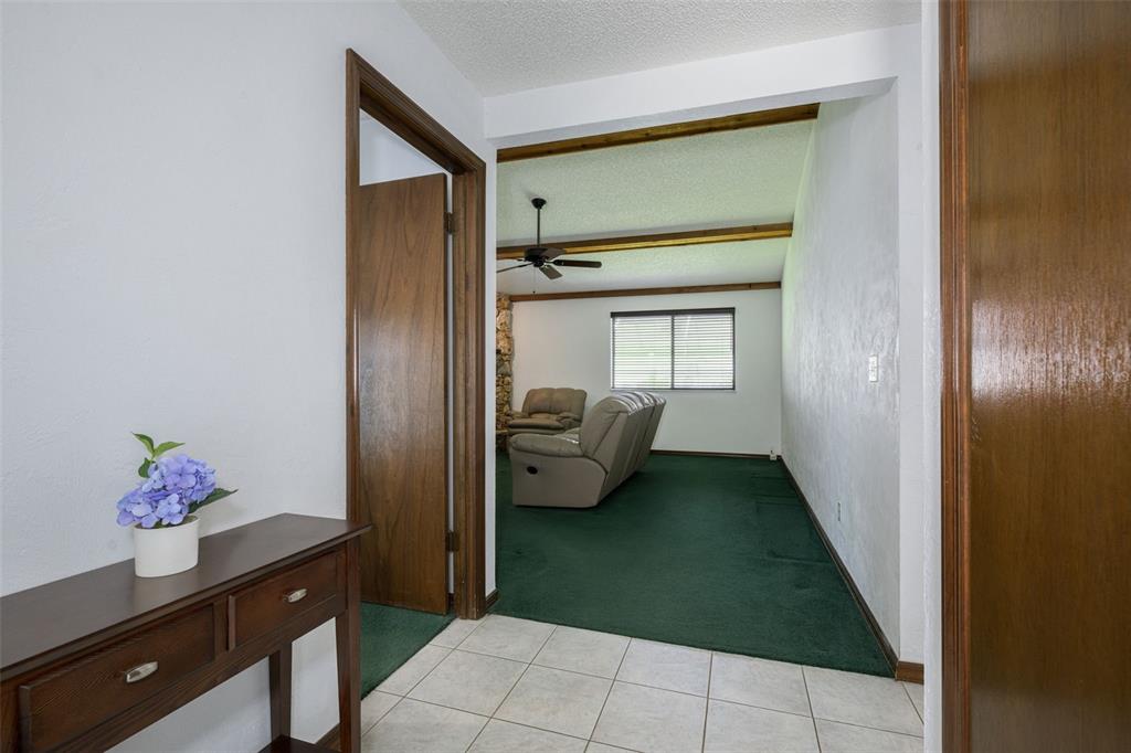 A tiled entryway leads into a living room with green carpeting and exposed ceiling beams — 1123 SHERBOURNE WAY, ORMOND BEACH, FL