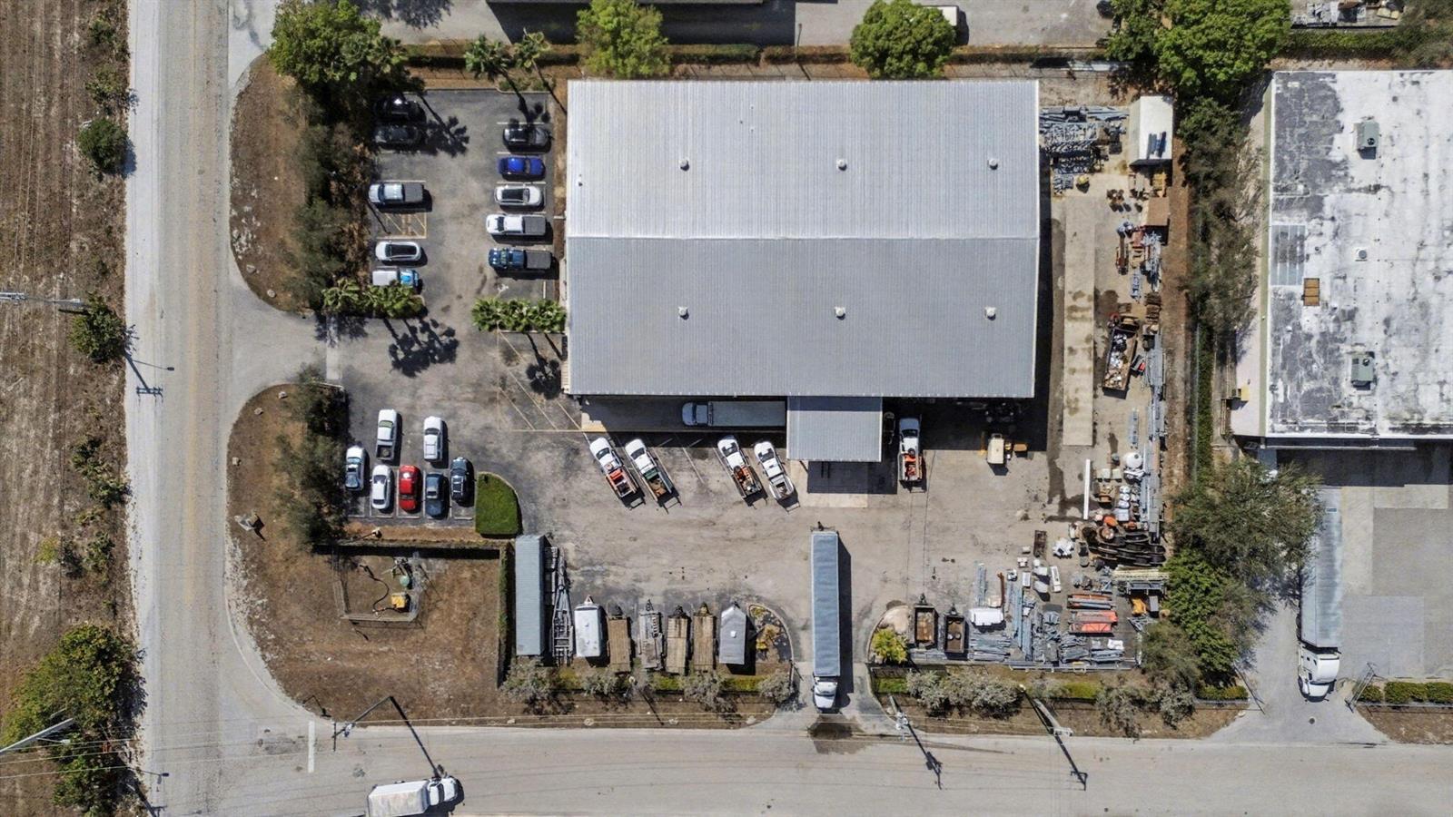 An aerial view shows a warehouse building with a parking lot and outdoor storage area — 6861 Garden Road, Riviera Beach FL 33404, RIVIERA BEACH, FL
