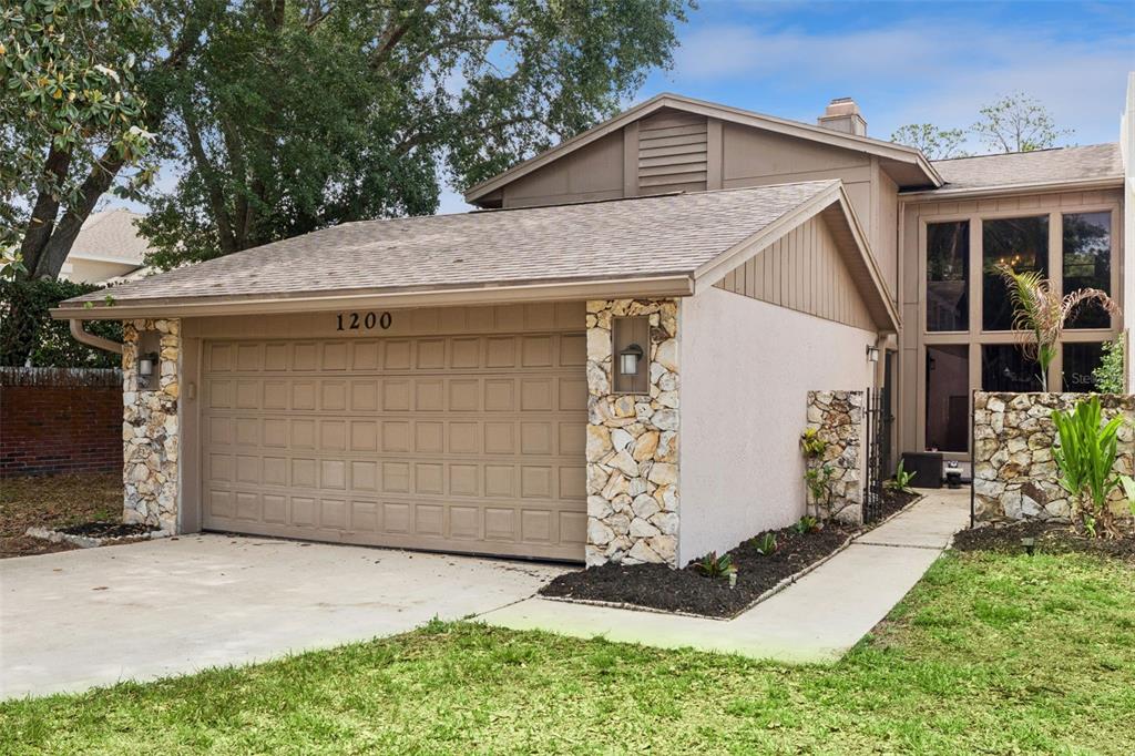 A house exterior features a two-car garage, stone accents, and a concrete driveway — 1200 ROYAL OAK DRIVE, WINTER SPRINGS, FL