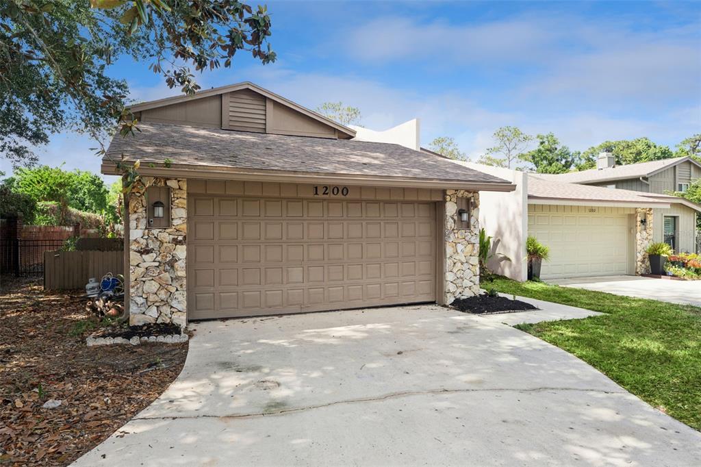 A concrete walkway leads through a stone-walled courtyard toward a tall, multi-pane window — 1200 ROYAL OAK DRIVE, WINTER SPRINGS, FL