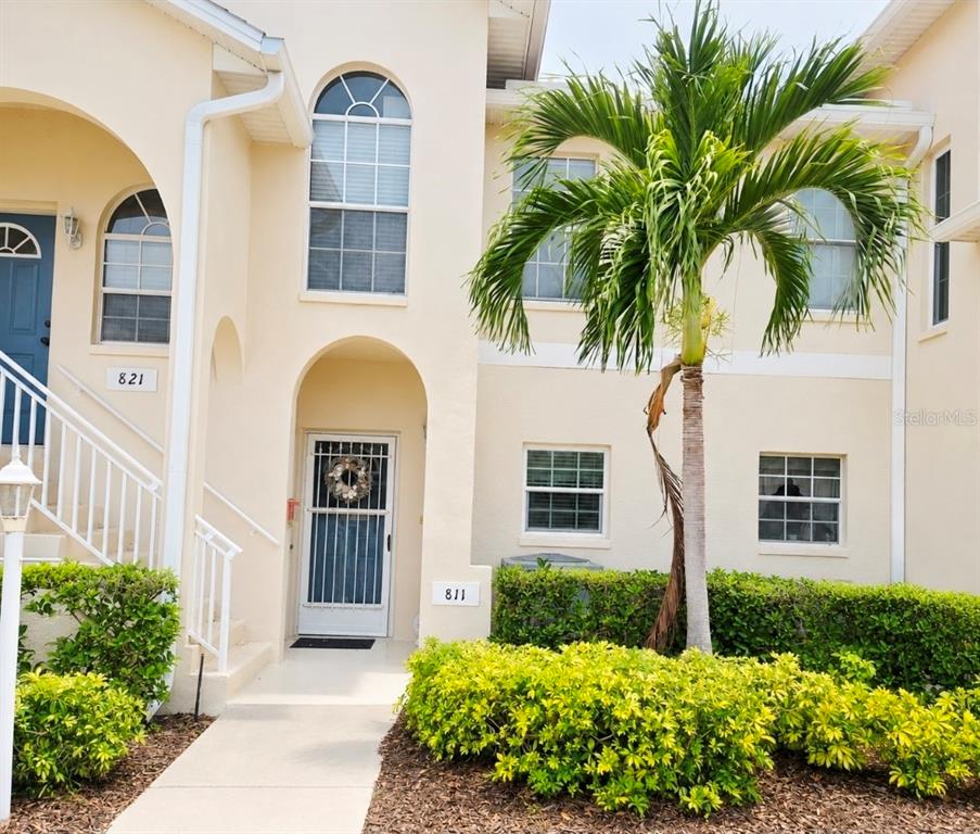 A two-story beige stucco building exterior features arched entryways, white railings, and a palm tree — 8360 WINGATE DRIVE UNIT 811, SARASOTA, FL