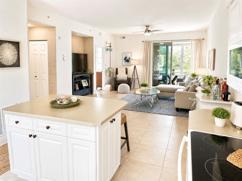 An open-concept kitchen island overlooks a living room with a sofa and sliding glass doors — 8360 WINGATE DRIVE UNIT 811, SARASOTA, FL