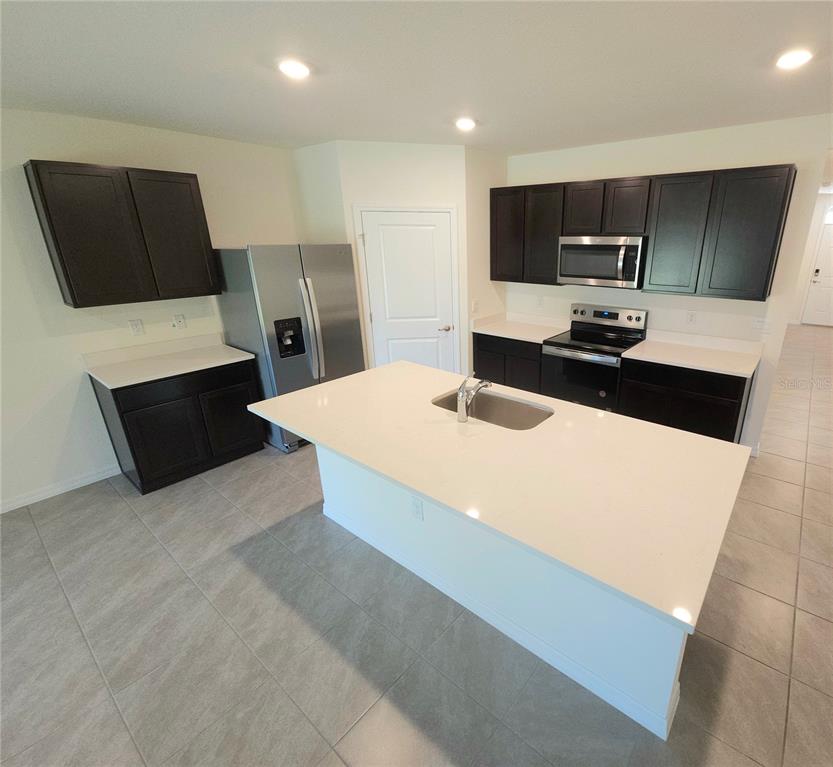 A kitchen features dark cabinets, stainless steel appliances, a white island, and light tile flooring — 296 HICKORY COURSE TRAIL, OCALA, FL