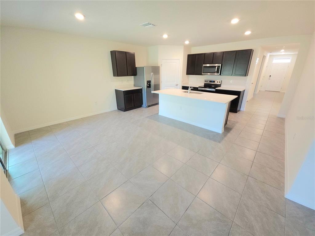 A kitchen features dark cabinetry, white countertops, a center island, and light-colored tile flooring — 296 HICKORY COURSE TRAIL, OCALA, FL
