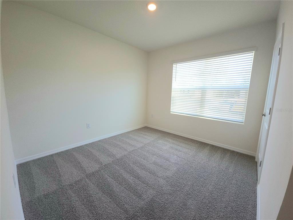 An empty bedroom features neutral walls, gray carpet, and a window with white blinds — 296 HICKORY COURSE TRAIL, OCALA, FL