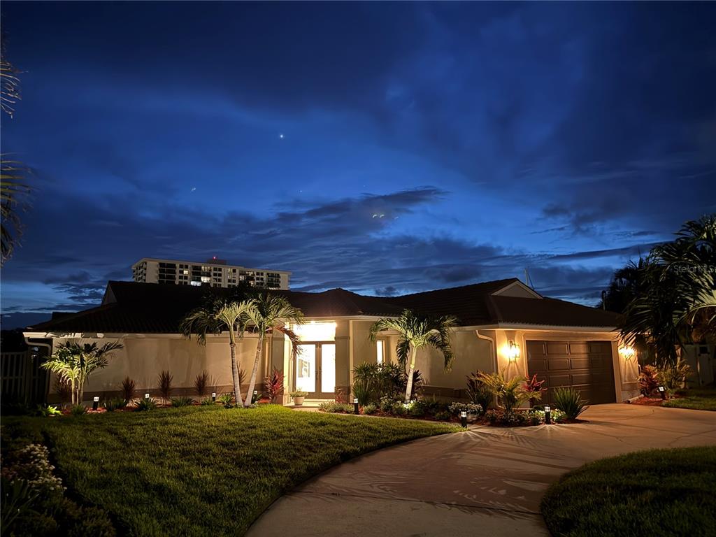 A single-story house with a driveway and palm trees at dusk under a cloudy sky — 324 LEEWARD ISLAND, CLEARWATER BEACH, FL