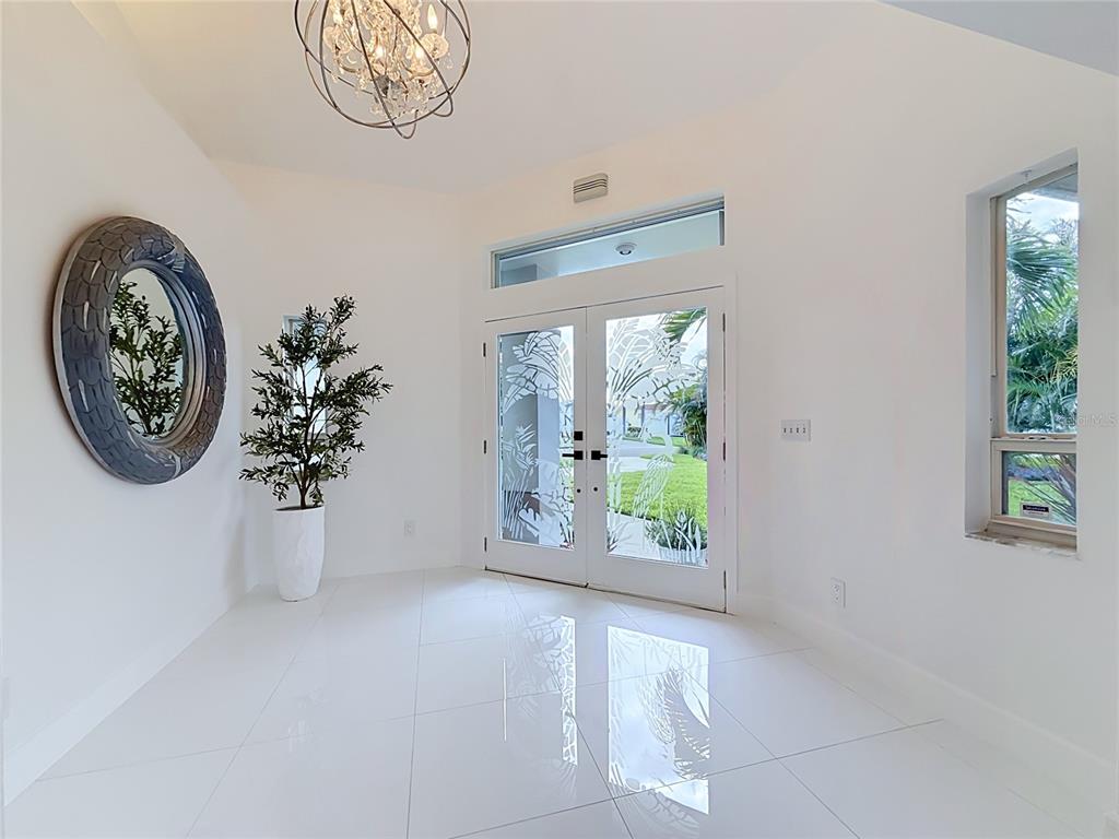 A bright entryway features white tile floors, a decorative mirror, and glass double front doors — 324 LEEWARD ISLAND, CLEARWATER BEACH, FL