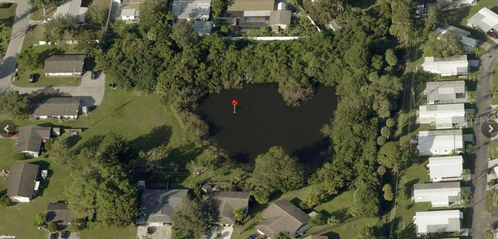 An aerial view shows a pond surrounded by trees and residential houses — ALGERIA COURT, BRADENTON, FL