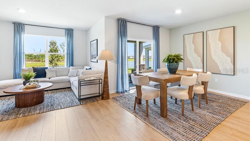 A bright living and dining area features light wood floors, neutral furniture, and blue curtains — 2027 VANDALIA PLACE, PARRISH, FL