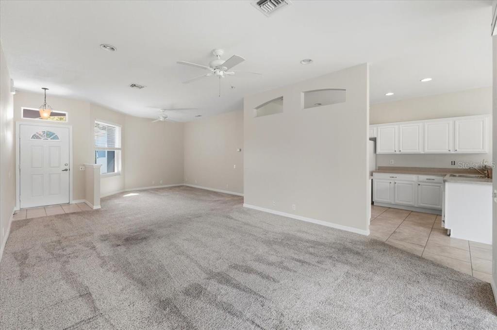 A living room with gray carpet leads to a kitchen with white cabinets and tile — 4050 WHISTLEWOOD CIRCLE, LAKELAND, FL