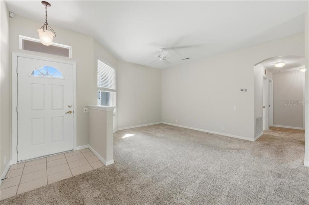 A living room features beige carpeting, neutral walls, a ceiling fan, and a tiled entryway — 4050 WHISTLEWOOD CIRCLE, LAKELAND, FL