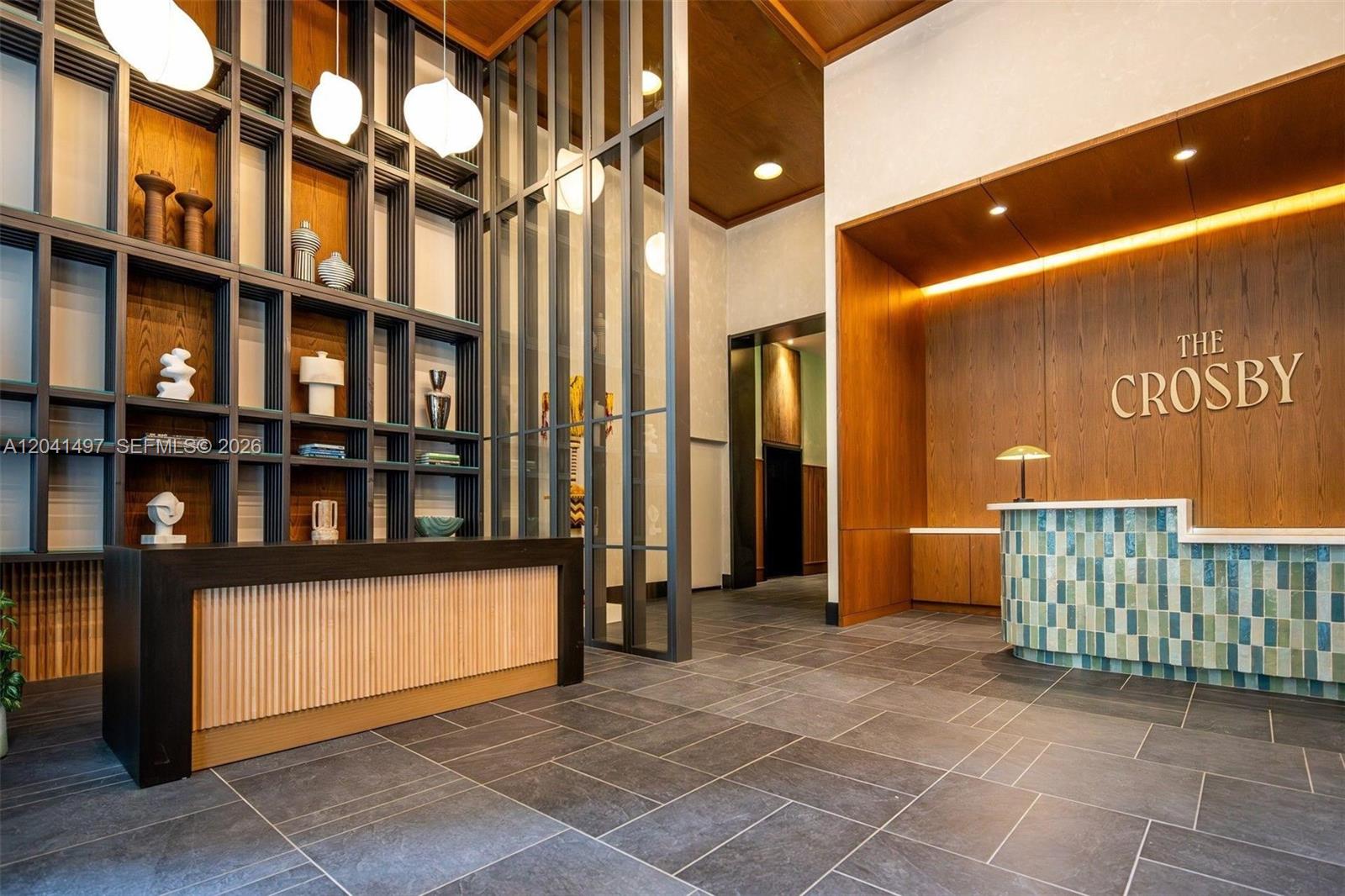 A modern lobby features a reception desk, wood-paneled walls, and a decorative shelving unit — 11 NE 6th St # 807, Miami FL 33132, MIAMI, FL