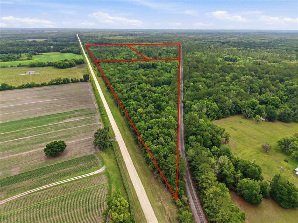 An aerial view shows a triangular wooded lot bordered by a road and railroad tracks — TBD NW 91ST STREET, ALACHUA, FL