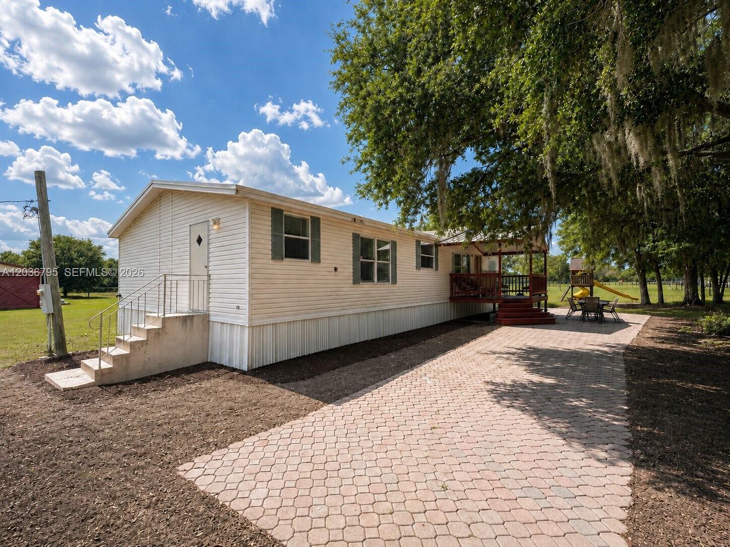 A single-story mobile home with white siding, a brick paver driveway, and a wooden deck — 1 Ridge Rd, Frostproof FL 33843, FROSTPROOF, FL