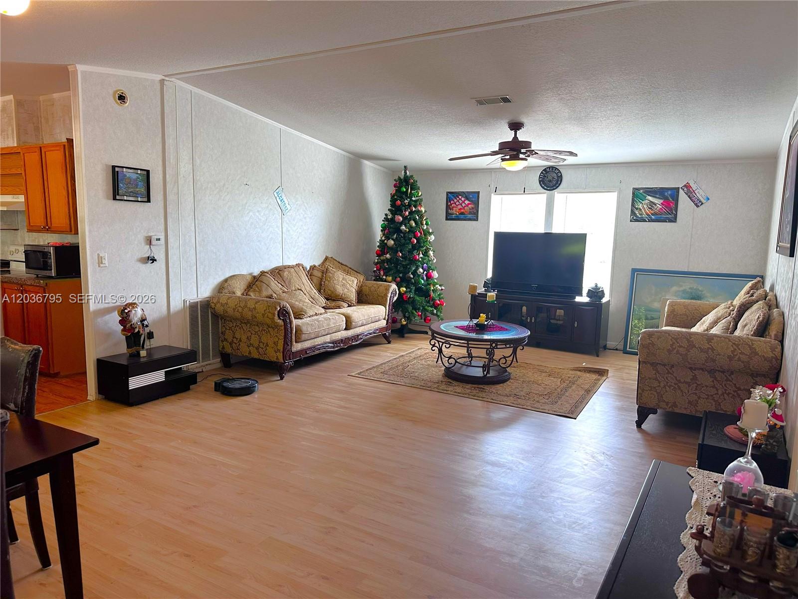 A living room features light wood flooring, two patterned sofas, a Christmas tree, and a television — 1 Ridge Rd, Frostproof FL 33843, FROSTPROOF, FL