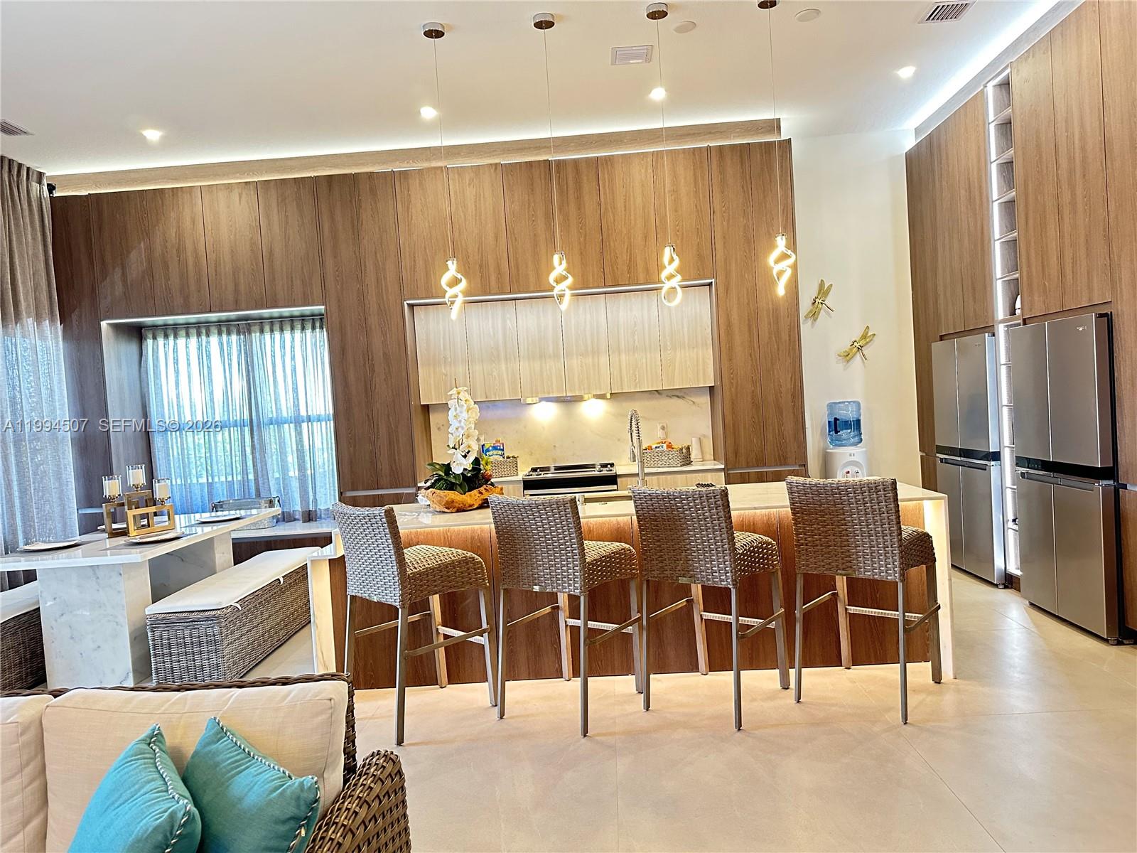 A modern kitchen features wood cabinetry, a marble island with bar stools, and pendant lighting — 4896 Corrado Ave, Ave Maria FL 34142, AVE MARIA, FL