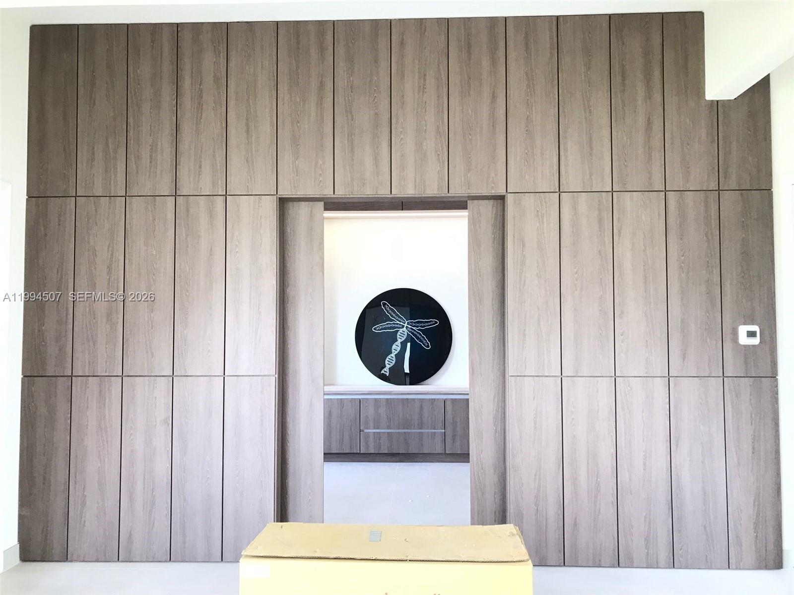 A wall of wood-paneled cabinetry features a central doorway leading to a room with artwork — 4896 Corrado Ave, Ave Maria FL 34142, AVE MARIA, FL