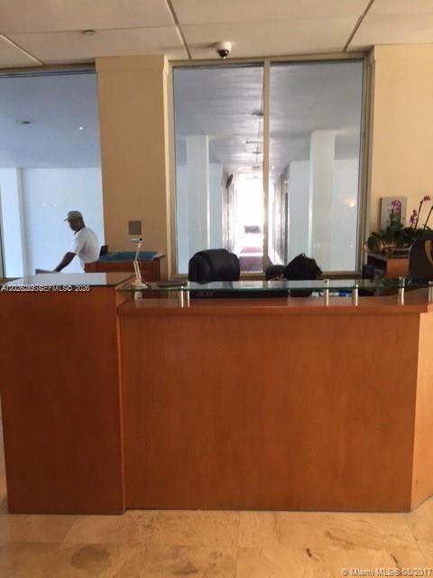 A wooden reception desk sits in a lobby with a person working behind it — 150 SE 25 RD # 15F, Miami FL 33129, MIAMI, FL