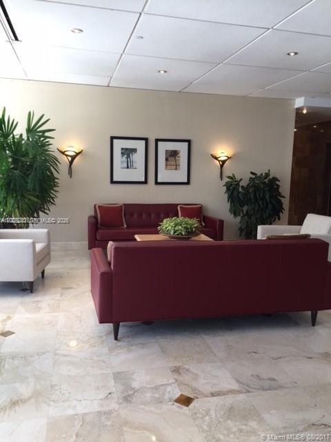 A lobby features two maroon sofas, white armchairs, and framed artwork on a beige wall — 150 SE 25 RD # 15F, Miami FL 33129, MIAMI, FL