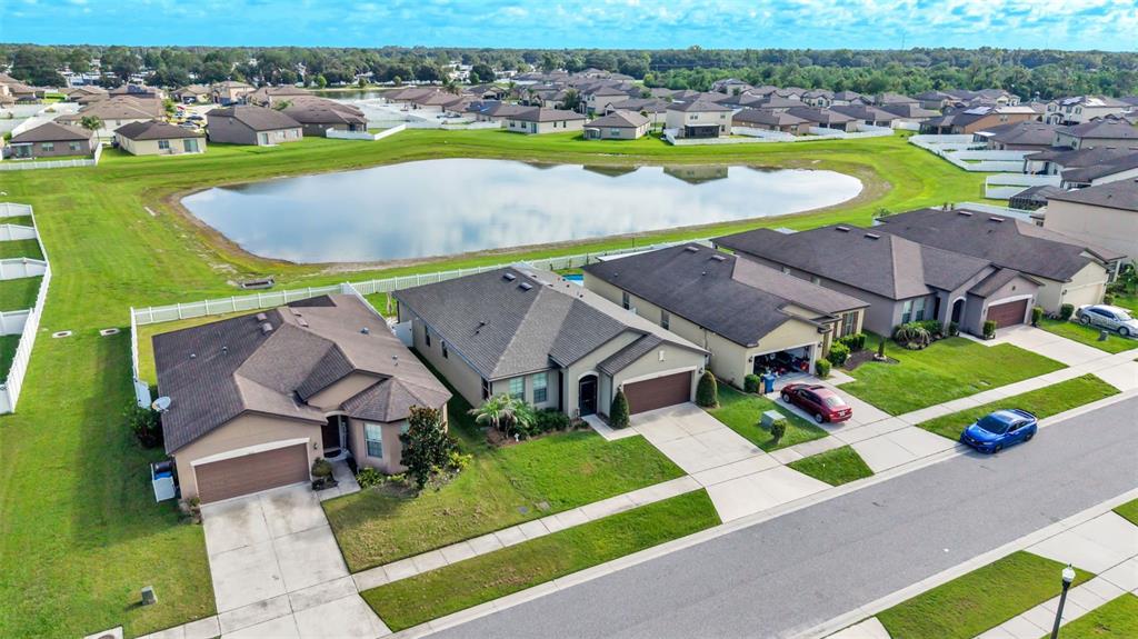 An aerial view shows suburban houses with driveways bordering a large retention pond — 8615 RINDGE ROAD, POLK CITY, FL