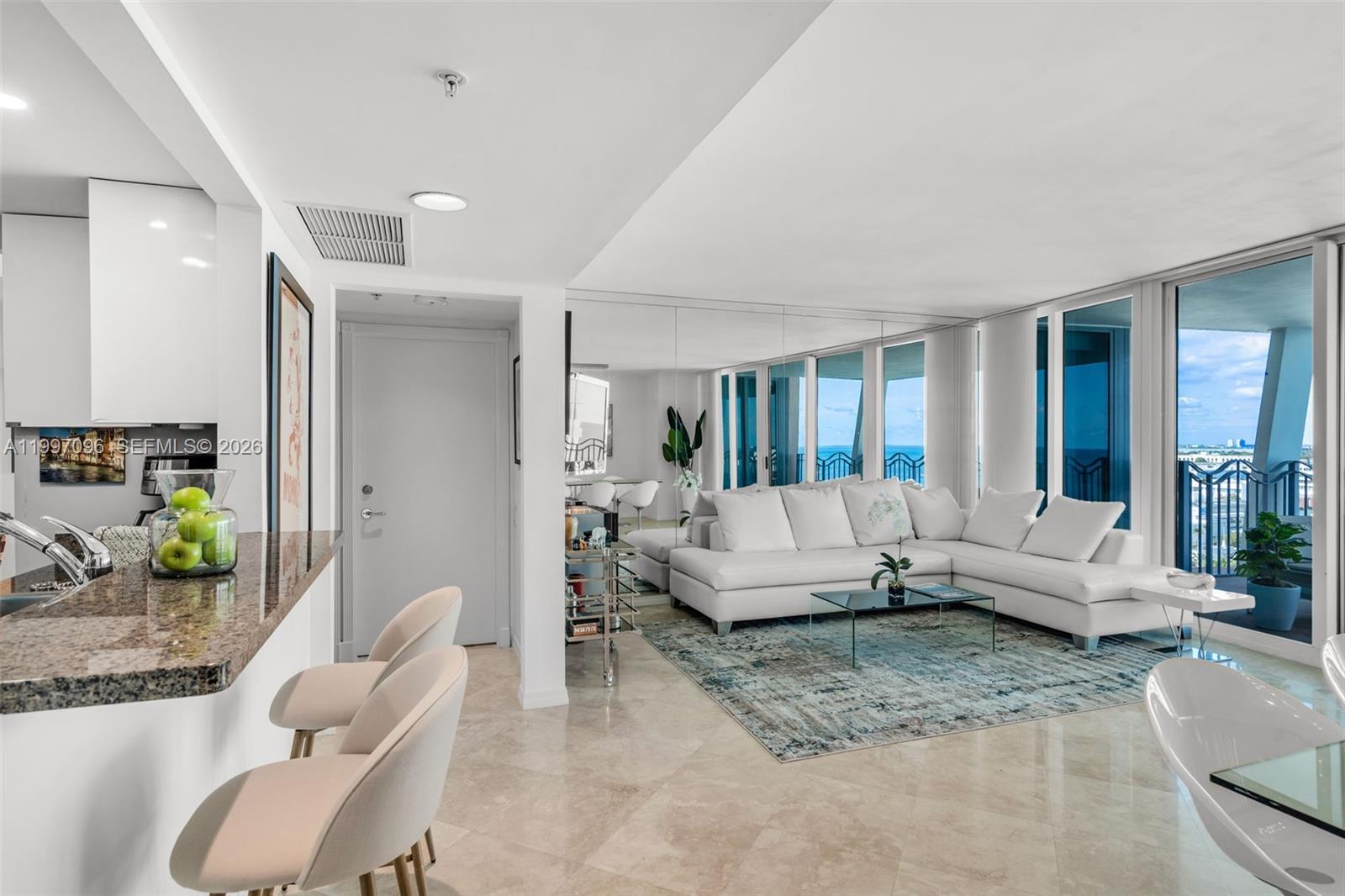A modern living room features a white sectional sofa, mirrored wall, and ocean view balcony — 1500 Ocean Dr # 05, Miami Beach FL 33139, MIAMI BEACH, FL