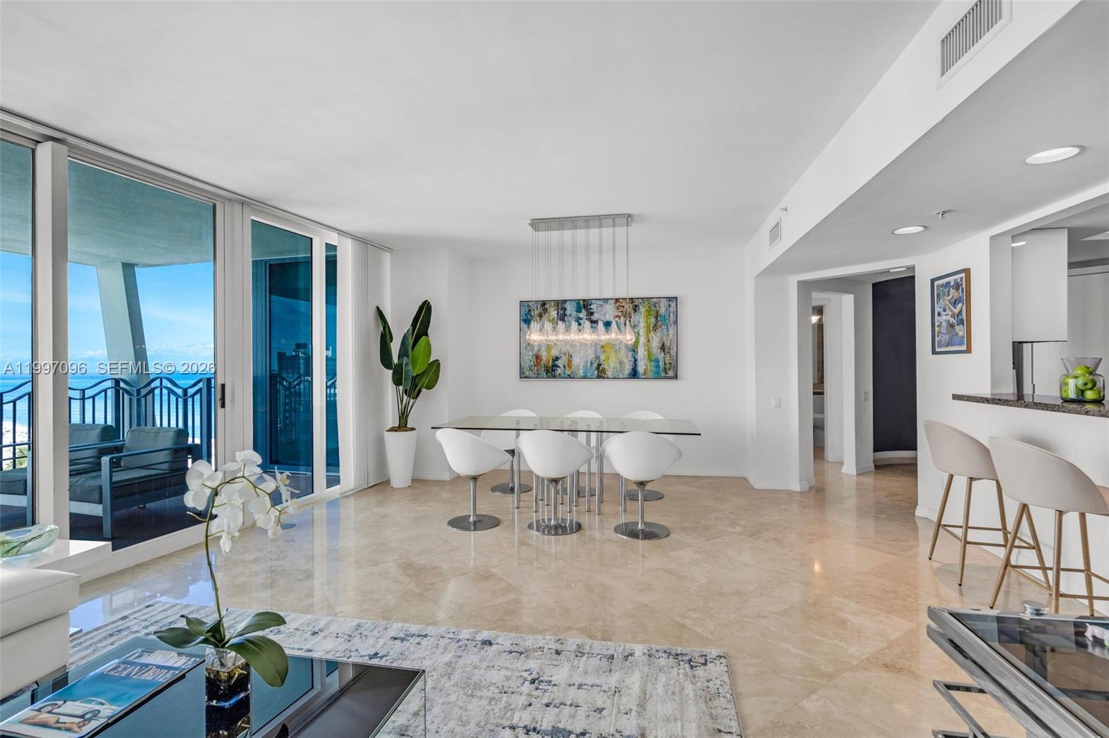 A dining area with a glass table and modern chairs sits beside a balcony view — 1500 Ocean Dr # 05, Miami Beach FL 33139, MIAMI BEACH, FL