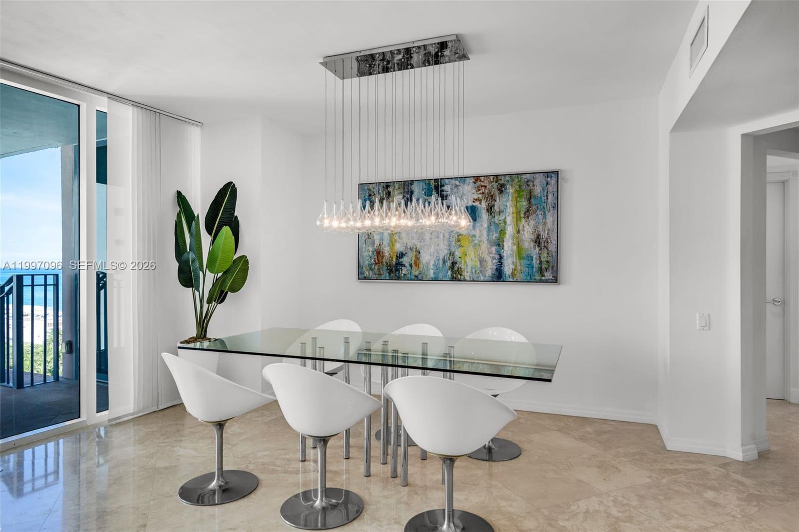 A dining room features a glass table, white swivel chairs, and a modern pendant light — 1500 Ocean Dr # 05, Miami Beach FL 33139, MIAMI BEACH, FL