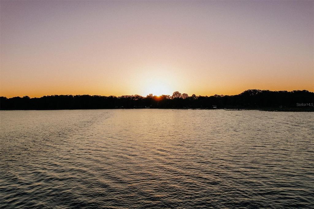 A sunset view over a calm lake with a treeline on the horizon — 13917 SE 204TH TERRACE, HAWTHORNE, FL