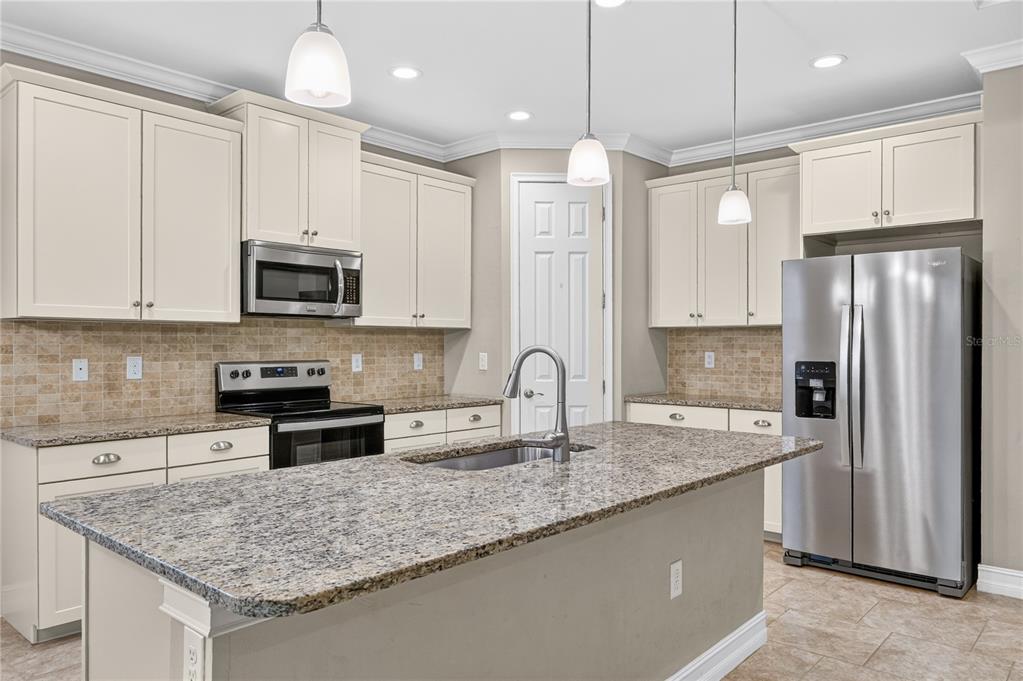 A kitchen features cream cabinets, granite countertops, a center island, and stainless steel appliances — 120 VENTOSA PLACE, NOKOMIS, FL