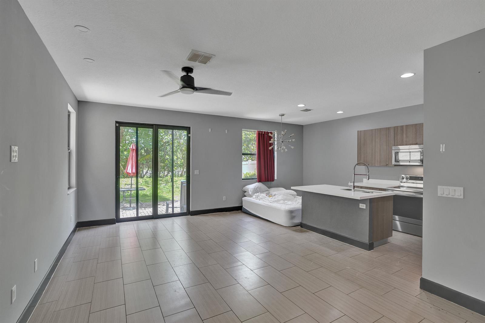An open-concept kitchen and living area features gray walls, tile flooring, and a sliding door — 5902 NW 46th Lane, Tamarac FL 33319, TAMARAC, FL