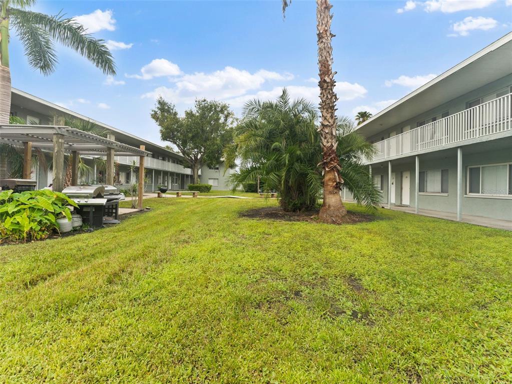 A grassy courtyard sits between two multi-story apartment buildings with palm trees and a grill — 335 47TH AVENUE N, ST PETERSBURG, FL