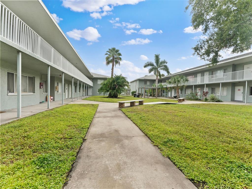 A concrete walkway leads through a grassy courtyard between two-story apartment buildings with balconies — 335 47TH AVENUE N, ST PETERSBURG, FL