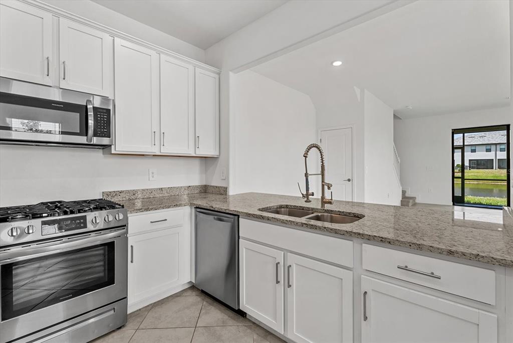 A kitchen features white cabinets, granite countertops, stainless steel appliances, and a view of water — 15245 LYLA TERRACE, LAKEWOOD RANCH, FL