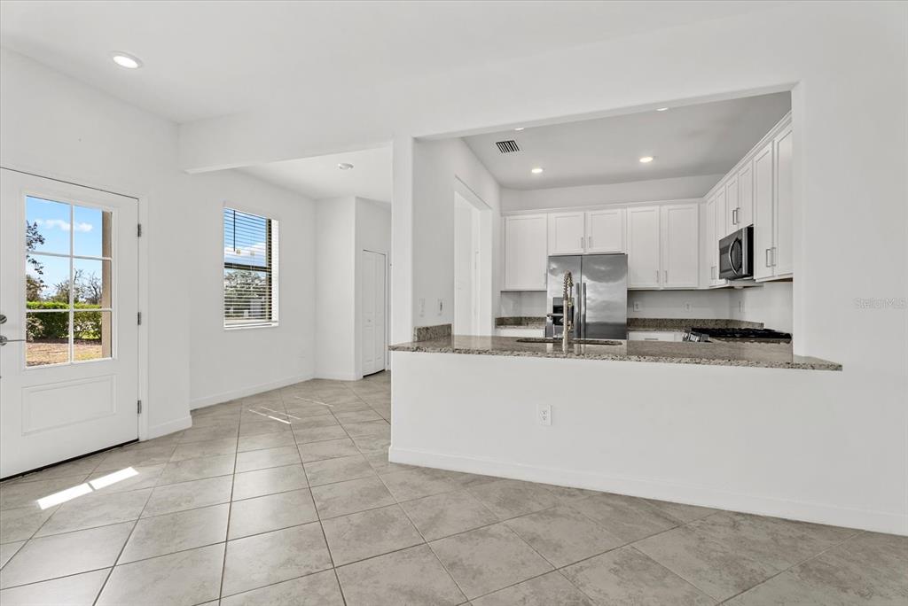 A kitchen with white cabinets and granite countertops overlooks a tiled dining area — 15245 LYLA TERRACE, LAKEWOOD RANCH, FL