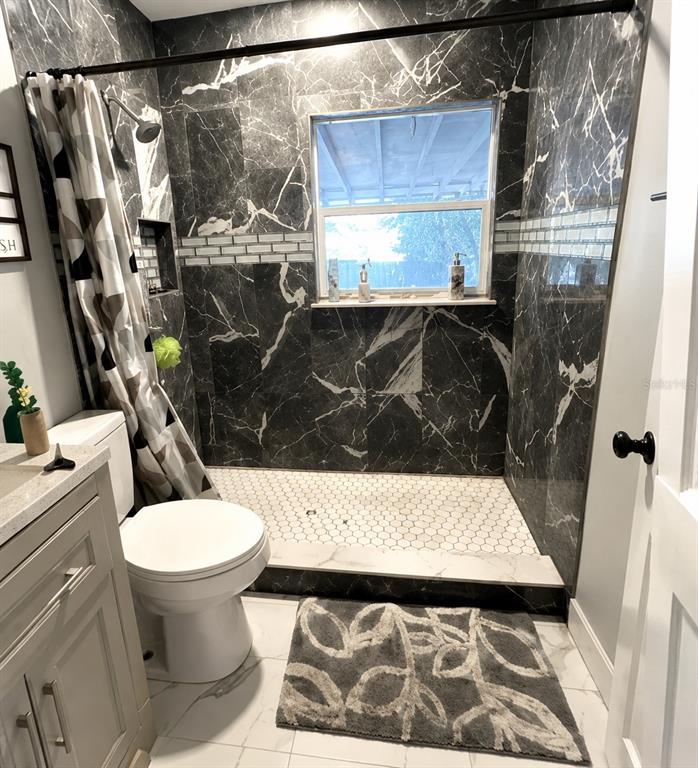 A bathroom features a walk-in shower with black marble-look tile, a white toilet, and vanity — 2400 S LAUREL AVENUE, SANFORD, FL