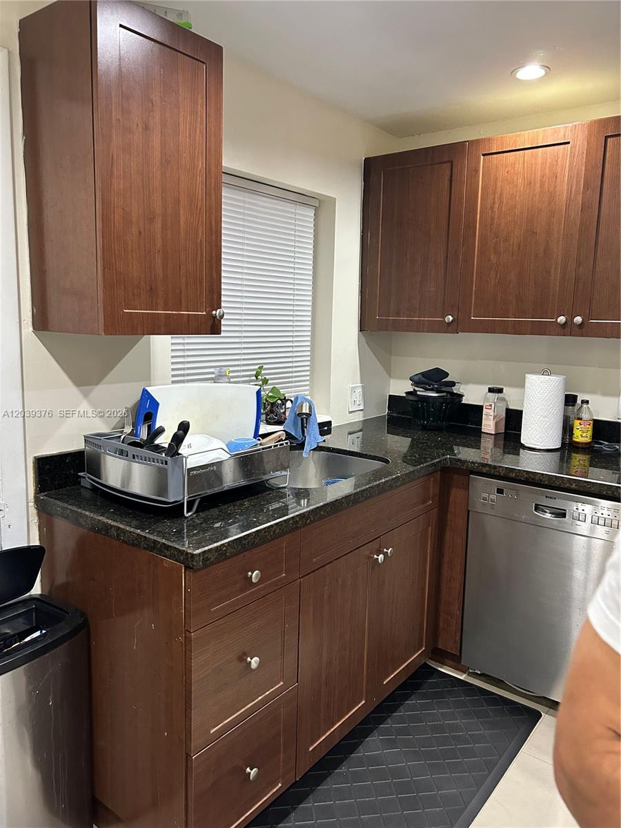 A kitchen features dark wood cabinets, black granite countertops, and a stainless steel dishwasher — NORTH MIAMI, FL