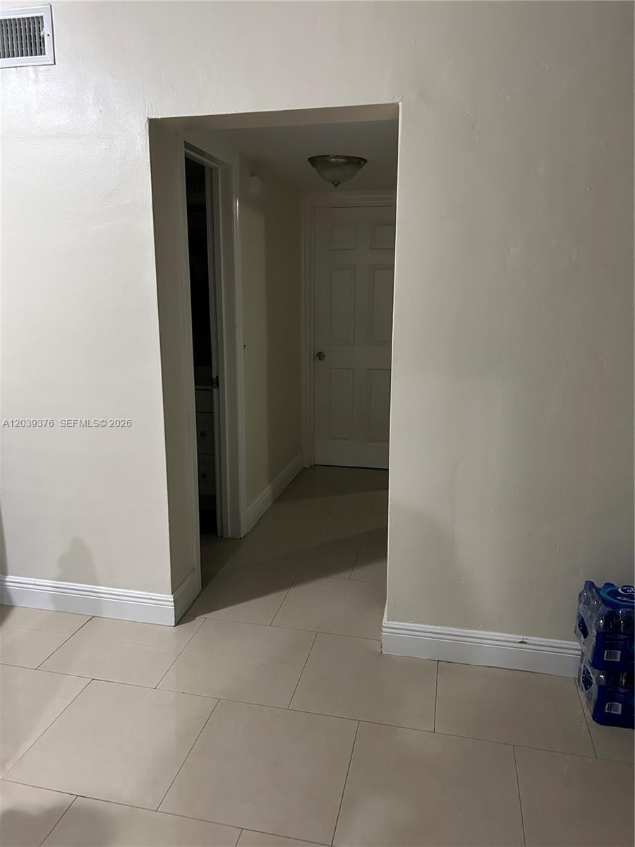 A hallway with light-colored tile flooring leads to a closed white door — NORTH MIAMI, FL