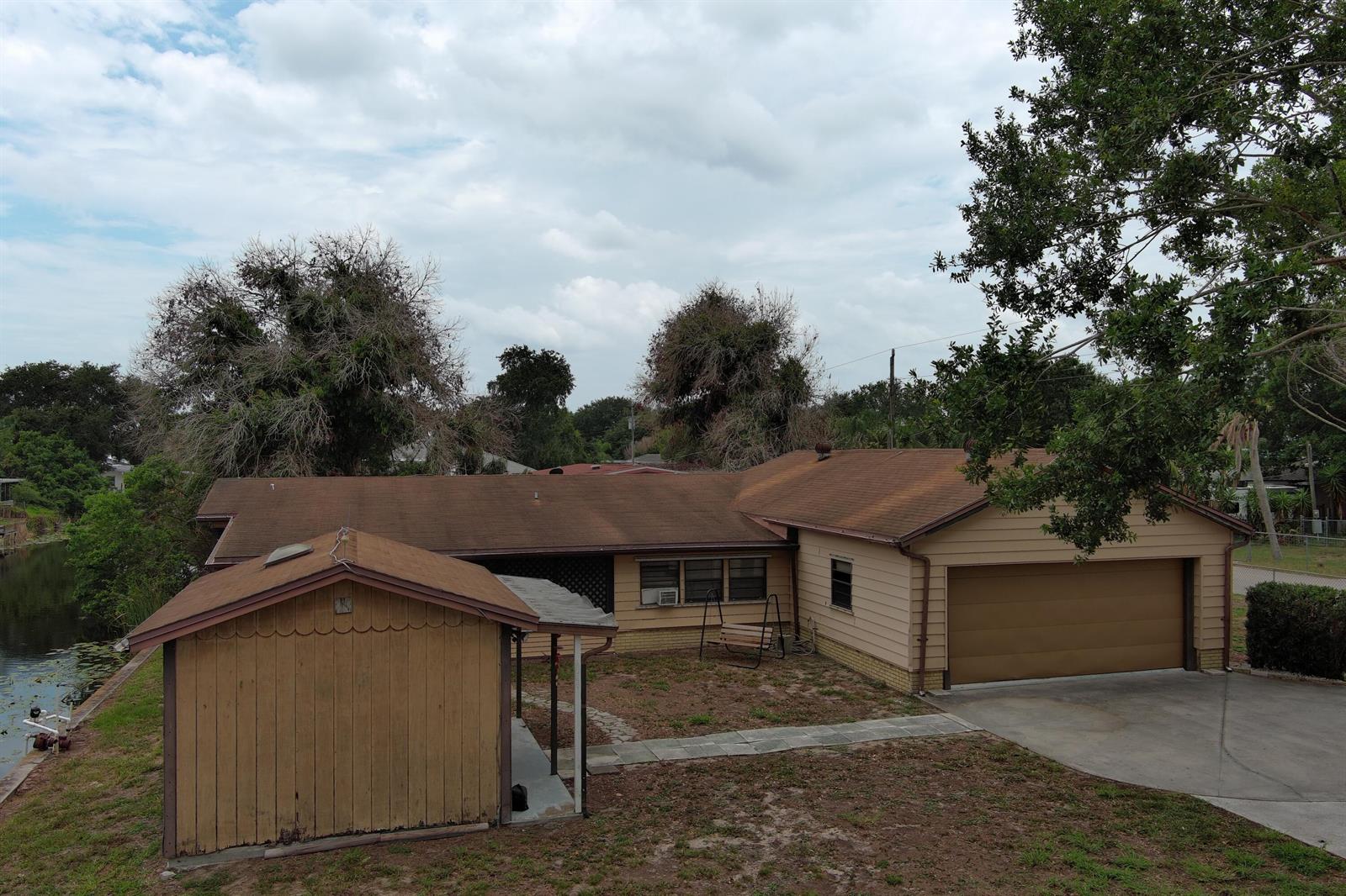 An exterior view of a single-story house with a garage, shed, and adjacent canal — 1013 9th Street, Okeechobee FL 34974, OKEECHOBEE, FL