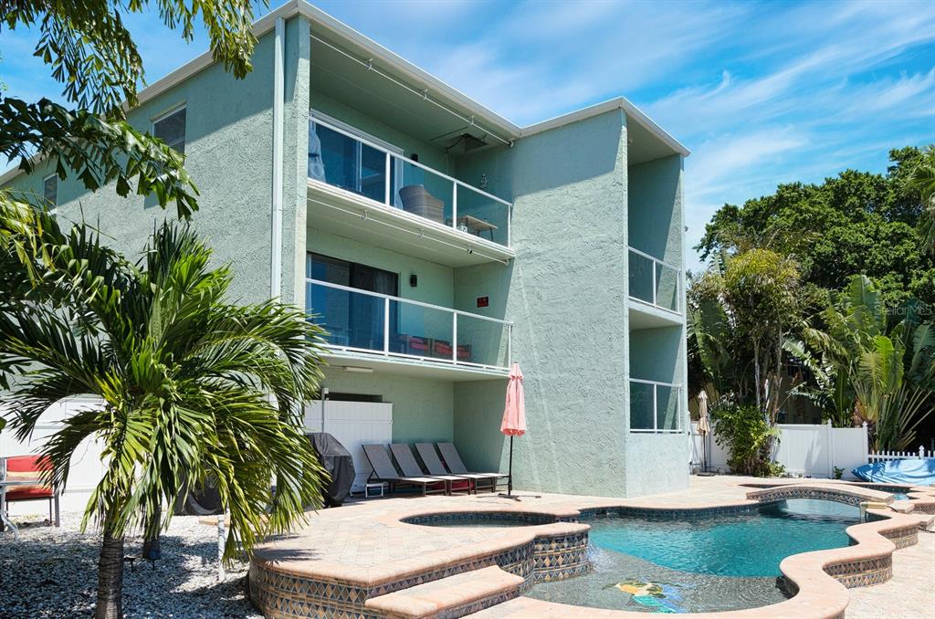 A three-story light green building with balconies overlooks a swimming pool and patio area — 125 110TH AVENUE UNIT 1, TREASURE ISLAND, FL