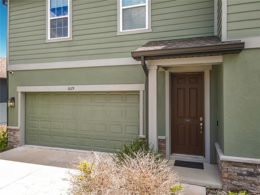 A two-story house exterior features a green garage, a brown front door, and stone accents — 1629 HILL PARK DRIVE, DELTONA, FL