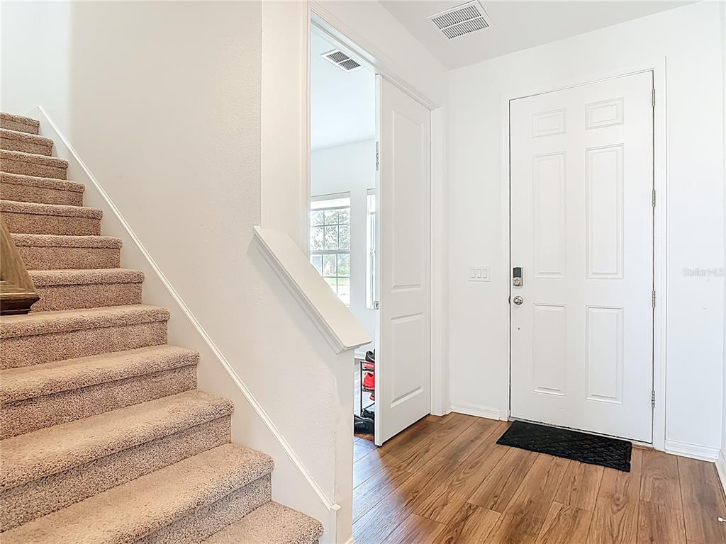 An entryway features a carpeted staircase, wood-look flooring, and a white front door — 1629 HILL PARK DRIVE, DELTONA, FL