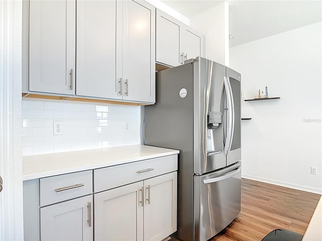 A kitchen features light gray cabinets, white countertops, a subway tile backsplash, and stainless appliances — 1629 HILL PARK DRIVE, DELTONA, FL