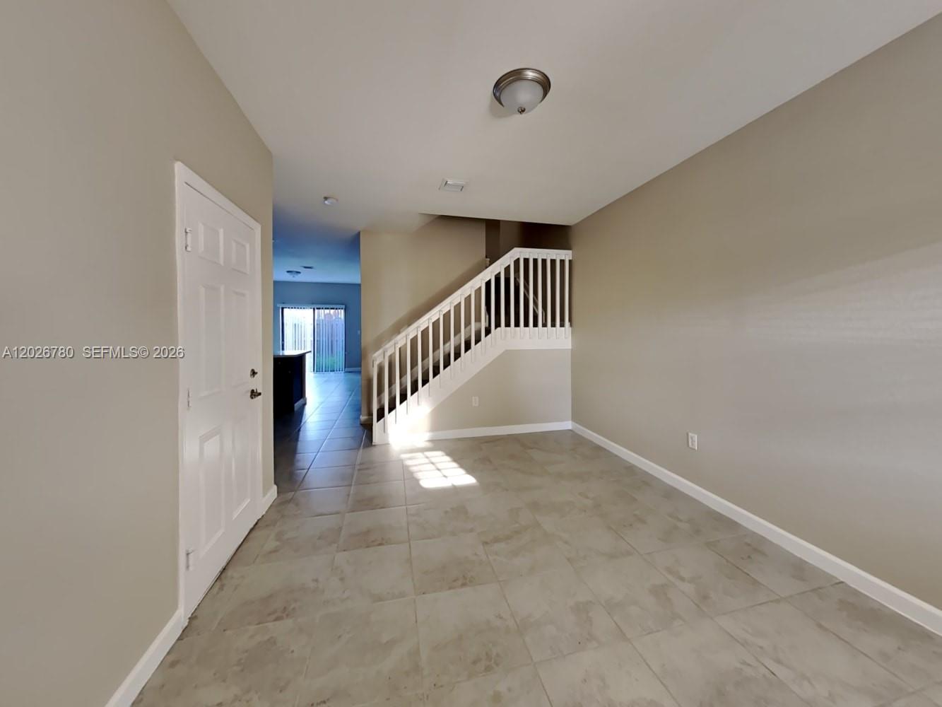 An entryway with tile flooring leads to a staircase with white railings and a door — HOMESTEAD, FL