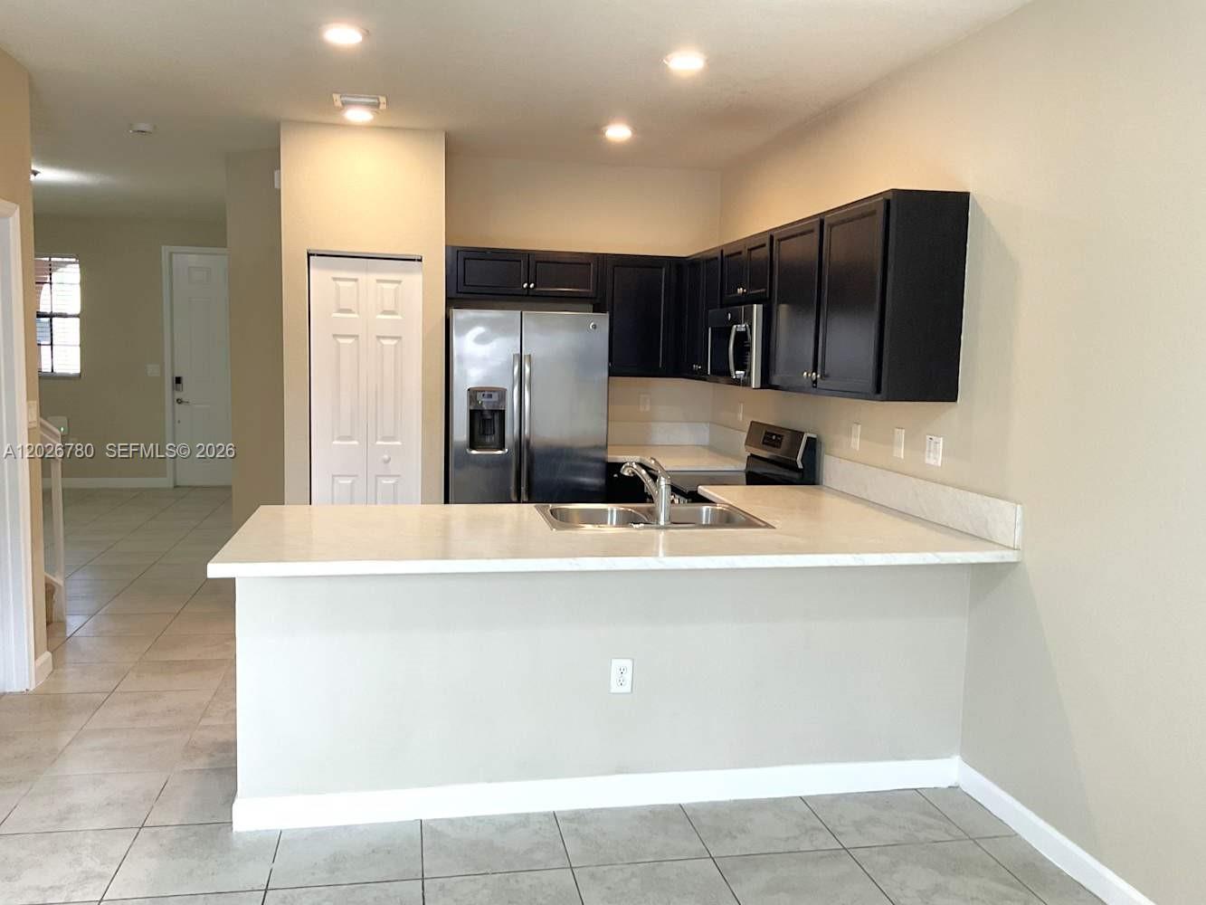 A kitchen features dark cabinets, stainless steel appliances, and a white countertop breakfast bar — HOMESTEAD, FL