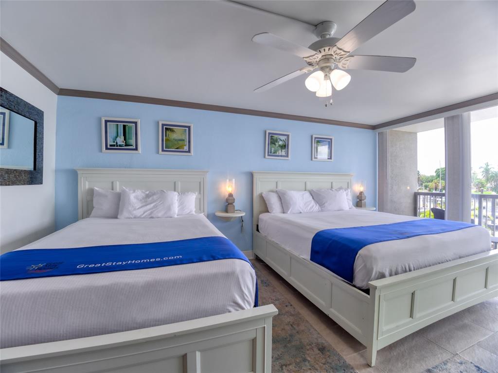A bedroom features two white beds, blue accent walls, a ceiling fan, and a balcony — 7150 N TAMIAMI TRAIL UNIT N409, SARASOTA, FL