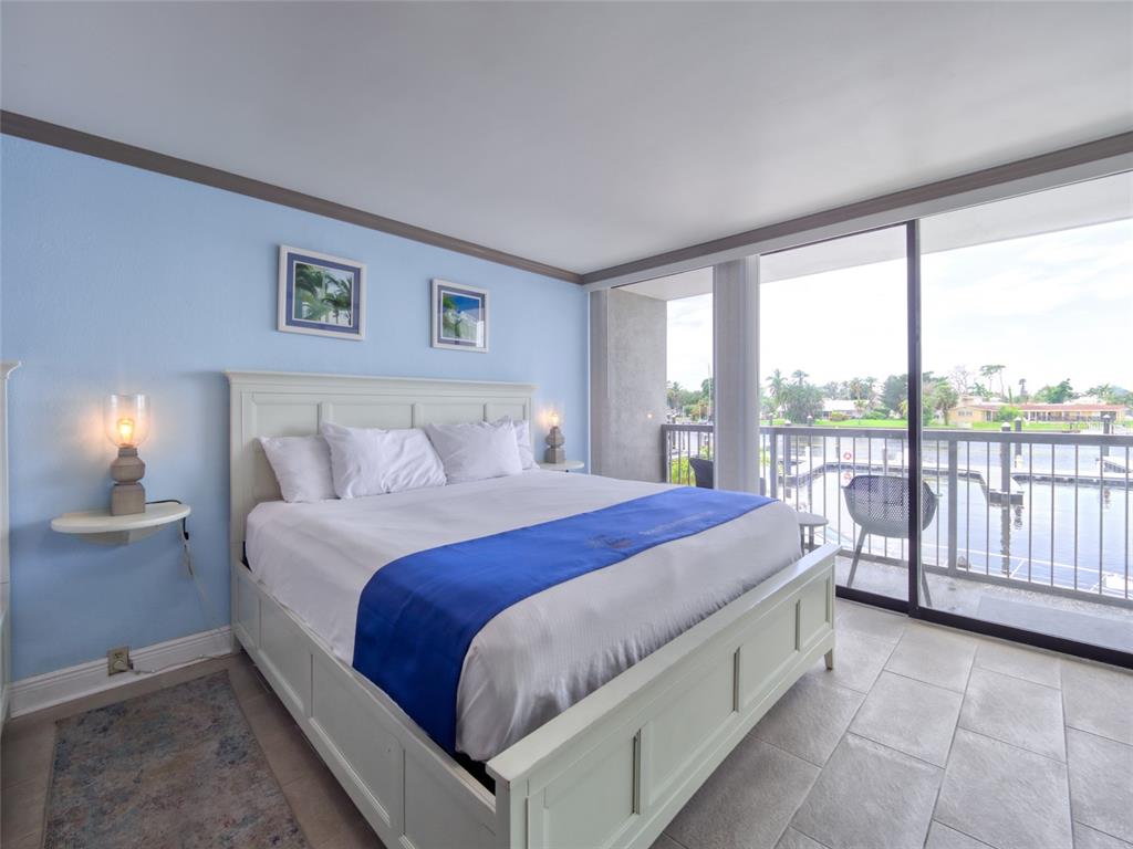A bedroom features a white bed, light blue walls, and a balcony overlooking a marina — 7150 N TAMIAMI TRAIL UNIT N409, SARASOTA, FL
