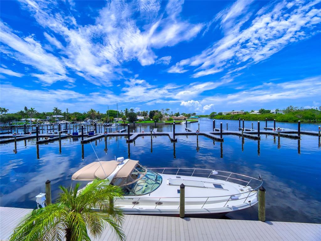 A white motorboat is docked at a wooden pier overlooking a calm canal and marina — 7150 N TAMIAMI TRAIL UNIT N409, SARASOTA, FL