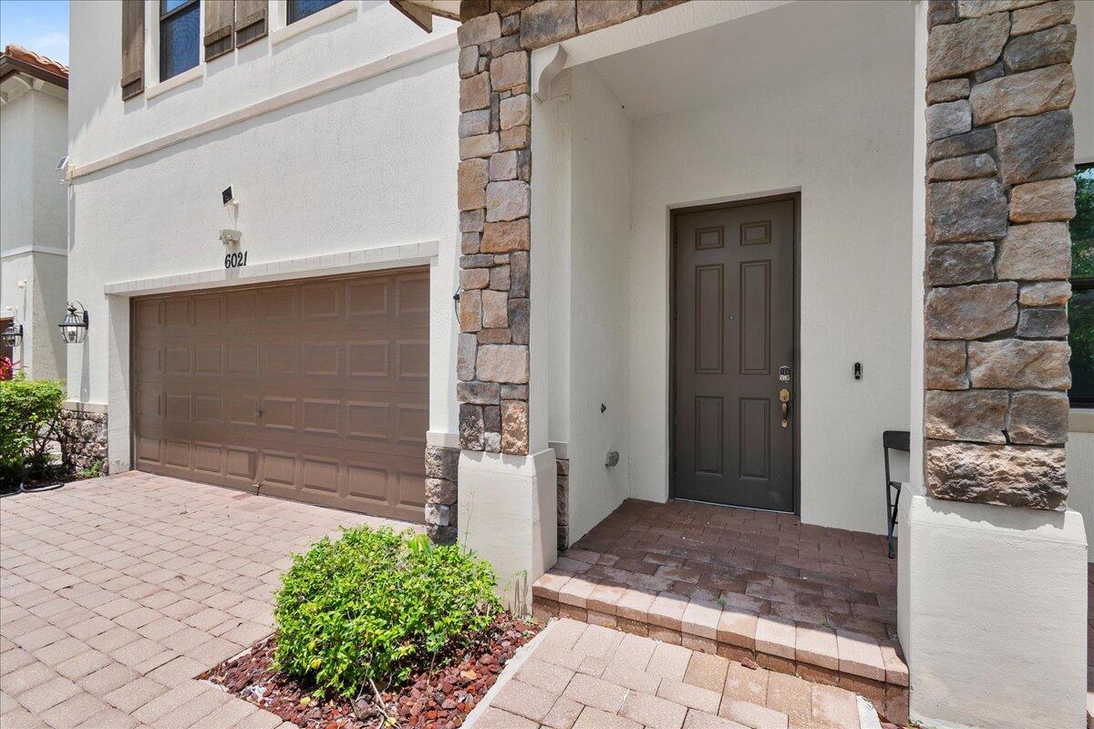 A residential exterior features a brown garage door, a front door, and stone pillar accents — 6021 Night Heron Court, FL 33415, FL